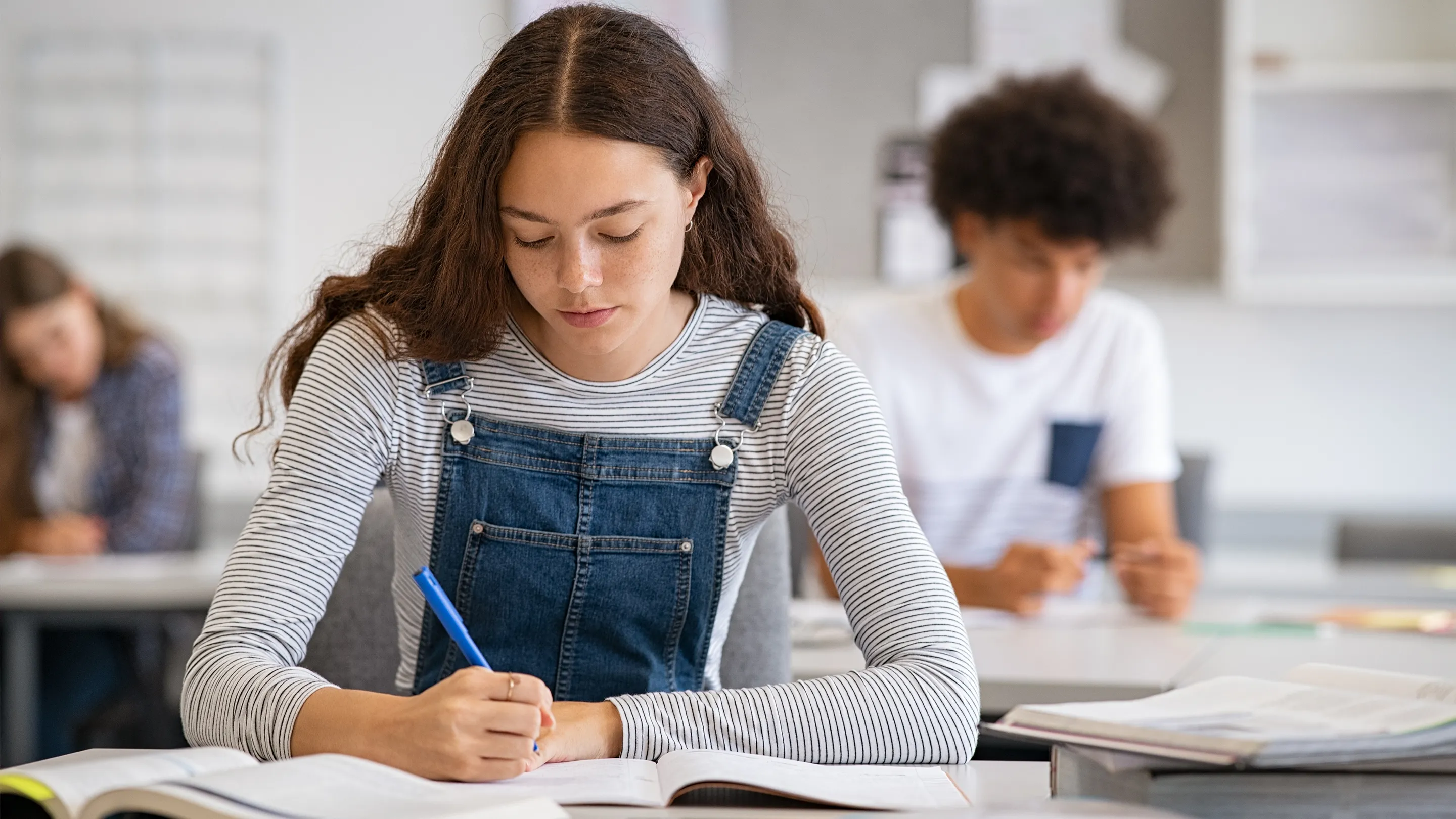 Student writing notes from a textbook in a classroom