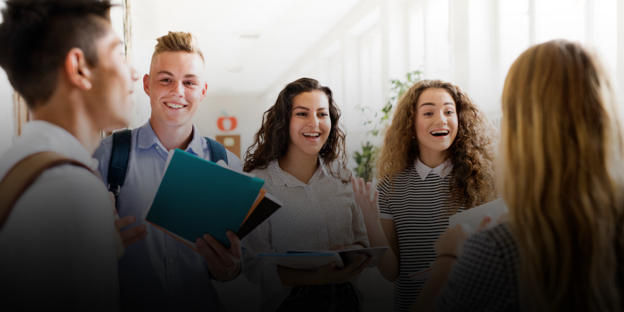 Group of students chatting and smiling in a school corridor holding folders